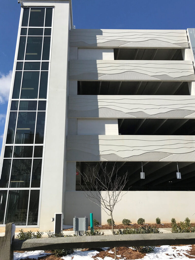 A detail of the exterior of the parking structure with the glass facade stair tower and decorative concrete panels visble