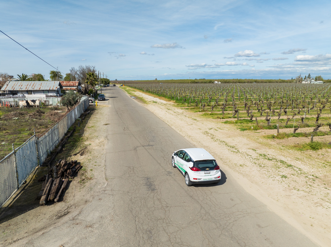 An EV microtransit vehicle drives on the edge of a small town, with farm fields on the opposite side of the road