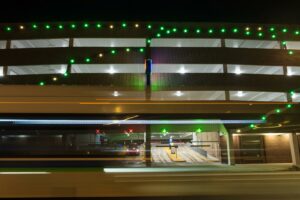 Exterior of North Capitol Ramp at night with architectural lighting and brightly lit entry/exit lanes visible behind a motion-blurred bus passing in the foreground