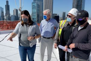 Sonia Surlej of Walker Consultants stands on the roof of a 54-story building and examines the progress of a roof replacement project with representatives from the manufacturer and contractor. Nearby skyscrapers and the Chicago skyline are visible in the background