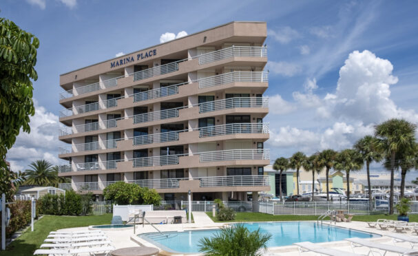 Marina Place Condominium, a pink stucco mid-rise building, with sunny blue skies and pool in the foreground