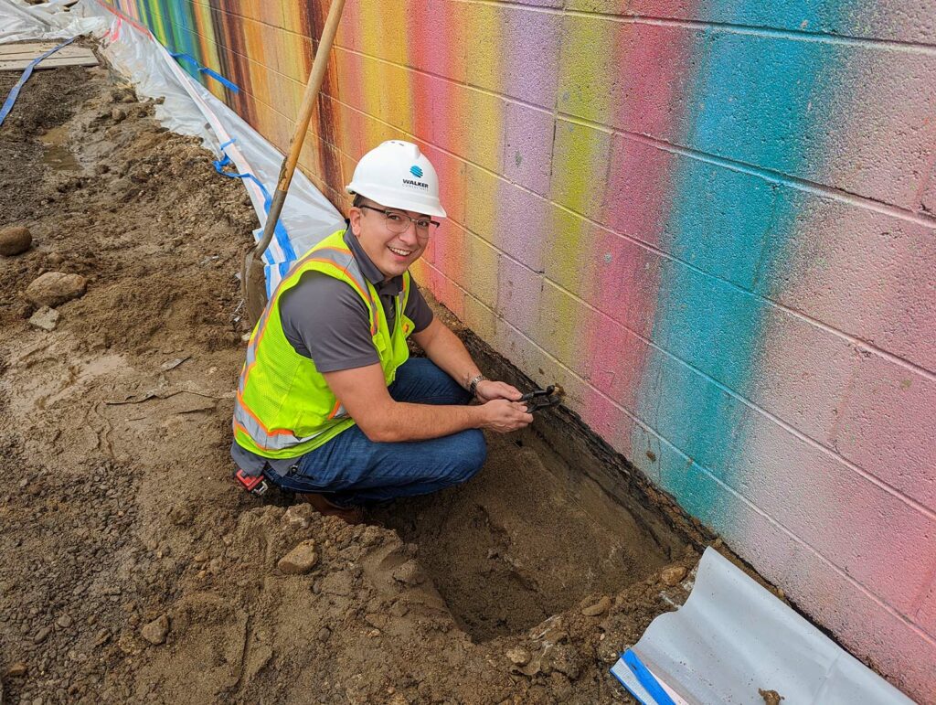 A Walker expert investigates the source of a leak on a colorfully painted exterior wall of a building